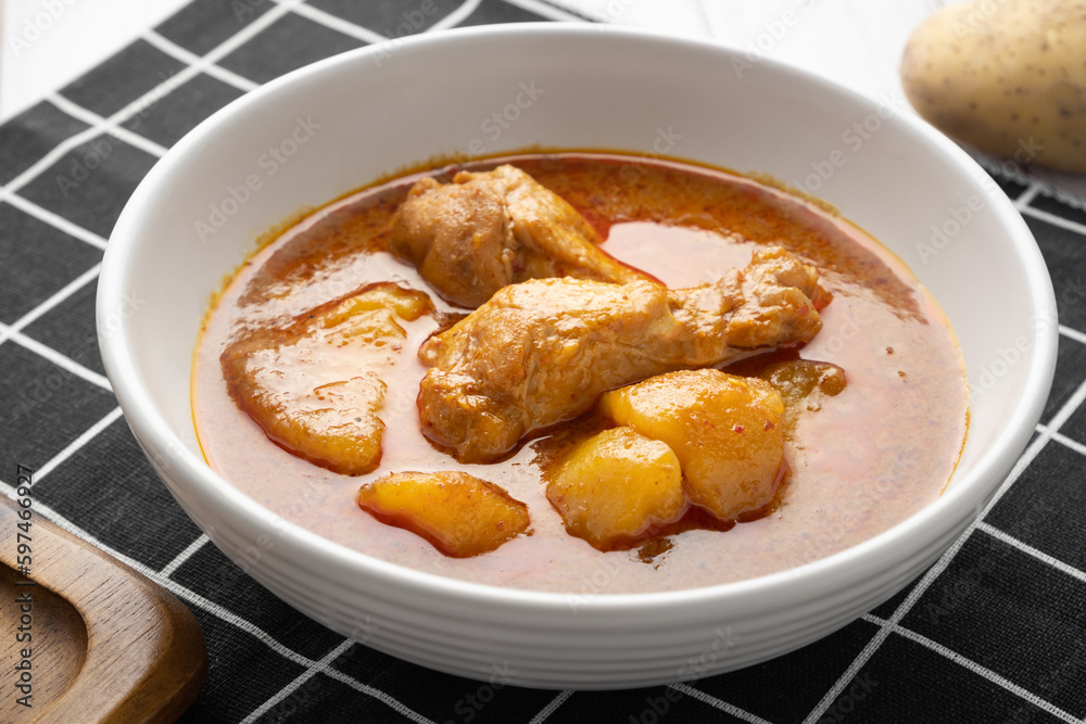 Chicken massaman with potato in white bowl on wooden table. Chicken massaman with potato in white bowl on wooden table.