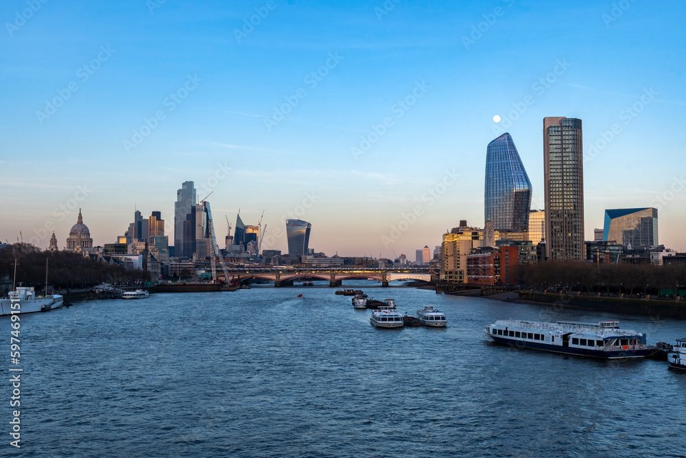 London skyline seen across the Thames at dusk with moon above skyscrapers