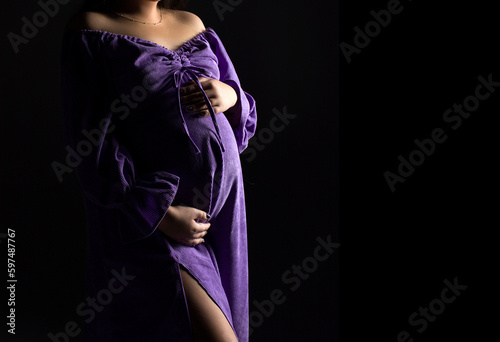 pregnancy woman in violet dress on a black background, studio pregnancy shoot