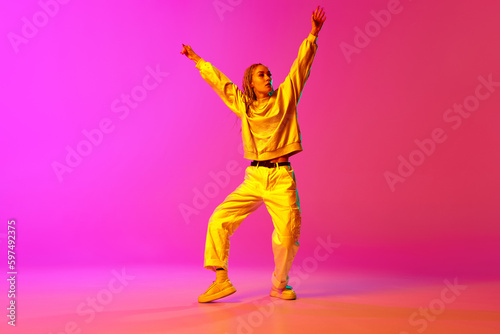 Portrait with one young girl  dancer with dreadlocks dancing with hands up over gradient pink background in neon light