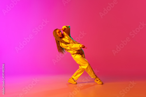 Portrait with professional dancer with dreadlocks wearing hip-hop stylysh clothes and dancing over gradient pink background in neon light