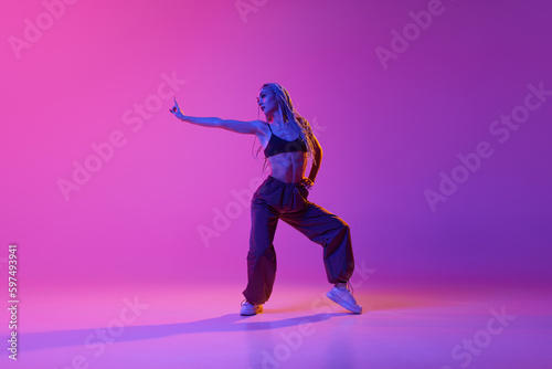 Portrait with one young girl  inspired dancer with pigtails dancing with hands over gradient purple background in neon light. Hip-hop