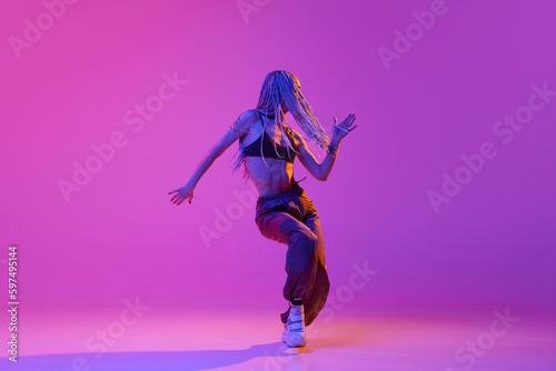 Portrait with one young girl, dancer with dreadlocks dancing over gradient purple background in neon light. Indoor training © Lustre Art Group 