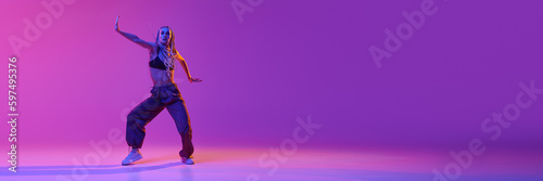 Portrait with young adorable girl dancing unusual movement over gradient purple background in neon light. Banner with copy space for text, ad