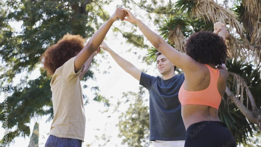 Carefree multiethnic friends raising arms up in park