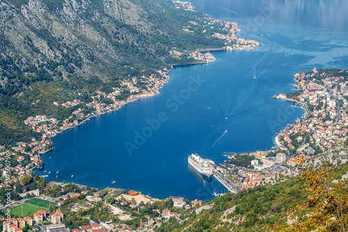 A panoramic aerial view of the Bay of Kotor, Monternegro with picturesque coastline, red roofs of houses and marina with boats and a large cruise ship..
