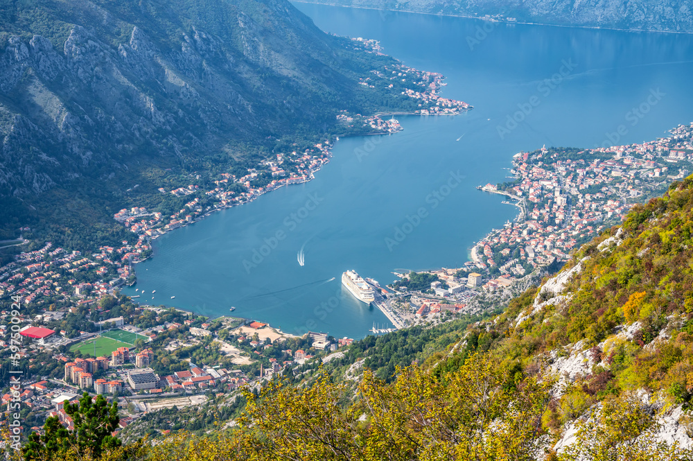 A panoramic aerial view of the Bay of Kotor, Monternegro with picturesque coastline, red roofs of houses and marina with boats and a large cruise ship..