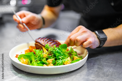 chef hand cooking Roasted Duck breast fillets with vegetable salad and batat in plate on restaurant kitchen