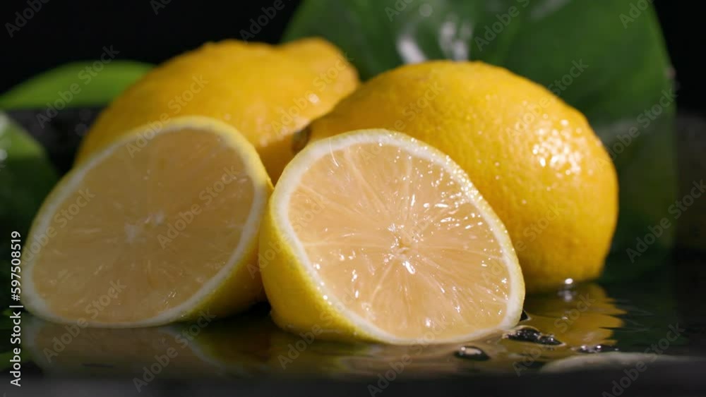 ripe lemon slice falls on citruses lying in water on a dark background, splashes scatter in different directions, close-up ripe lemon slice falls on citruses lying in water on a dark background, splashes scatter in different directions, close-up
