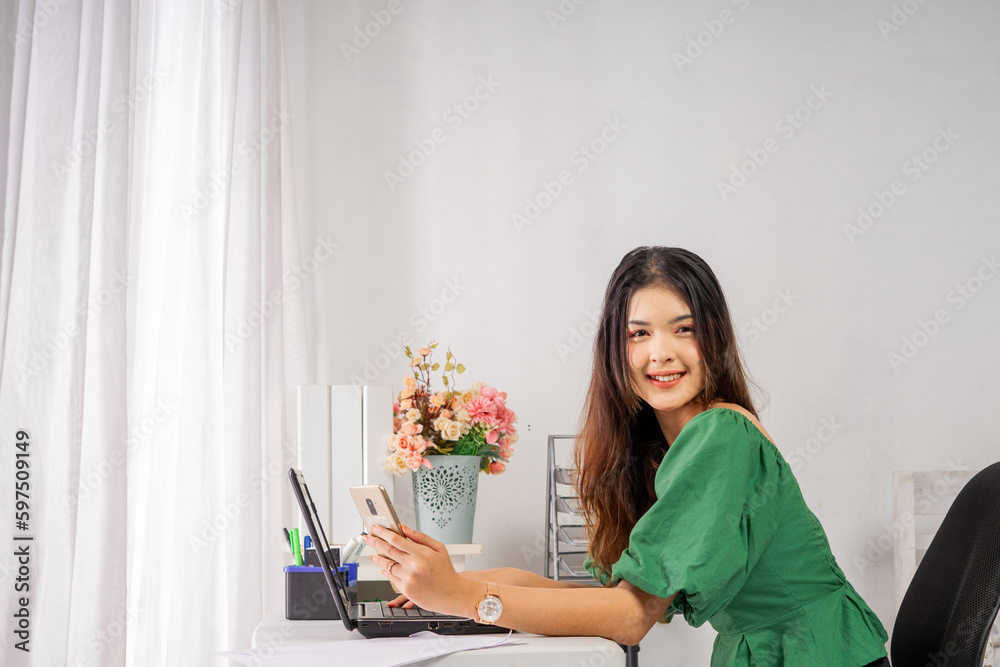 Beauty young Asian business female smiling to the camera while sitting and holding the mobile phone Beauty young Asian business female smiling to the camera while sitting and holding the mobile phone