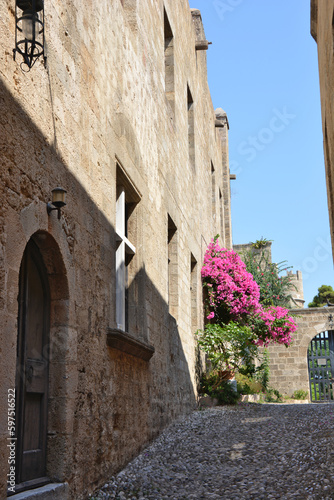 Fototapeta Naklejka Na Ścianę i Meble -  A street in the old town of Rhodes island in Greece with pink flowers on background