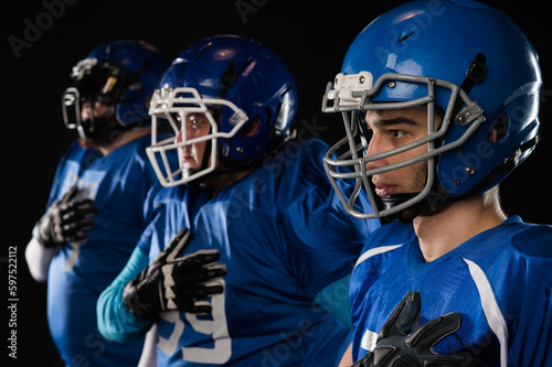Portrait of three men in blue uniforms for American football with a hand on his chest on a black background.