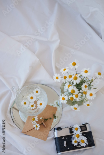 A bouquet of daisies in a glass vase and an old camera on a white bed.