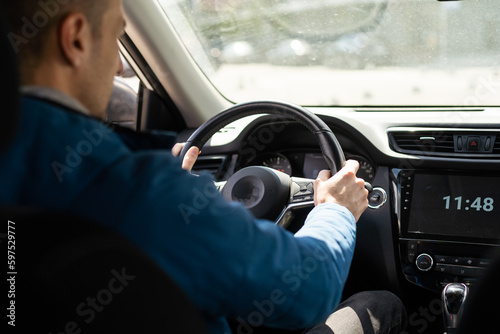 Handsome man in his 30s sitting in the driver's seat and smiling. Taxi driver listening to music on the car and changing the radio station. © Angelov