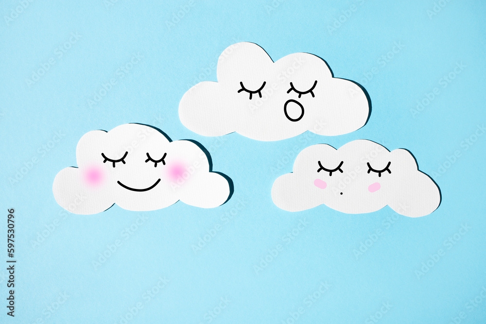 Sleeping clouds with funny faces on a blue background. The concept of a healthy baby sleep. Flat lay, top view, copy space.