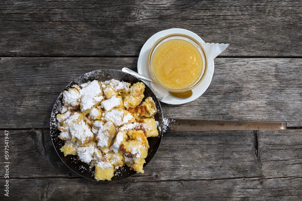Kaiserschmarrn in eiserner Pfanne mit Apfelbrei auf einem Holztisch ...