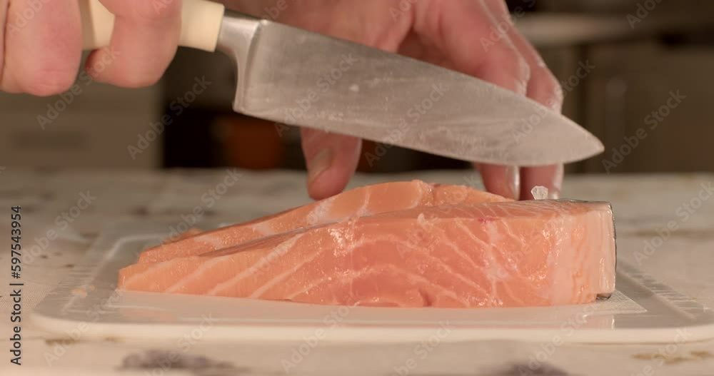 Slicing red salmon with a sharp knife in the kitchen by the hands of a cook. Preparing fish for servings. Fatty fatty overlays of the pulp of the raw product. Slicing red salmon with a sharp knife in the kitchen by the hands of a cook. Preparing fish for servings. Fatty fatty overlays of the pulp of the raw product.