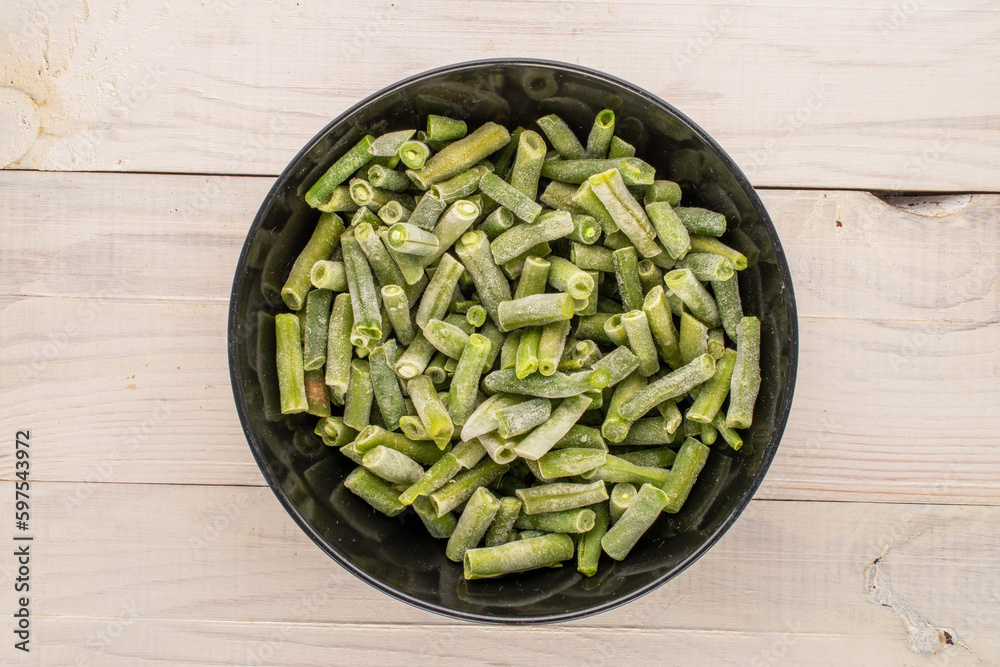Frozen green beans in a black ceramic plate  on a wooden table, macro, top view.