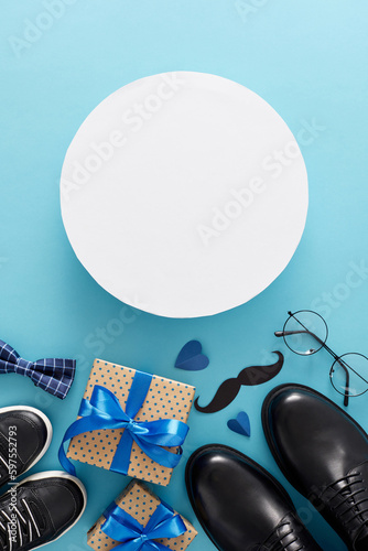 Happy Father's Day concept. Top view vertical flat lay of gift boxes, trendy shoes father and child, mustache, bow tie, glasses and hearts on light blue background with blank circle for greeting text