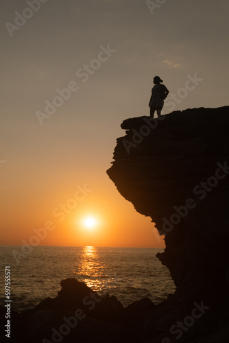 silhouette of woman on a rock, watching the sunset in the sea 