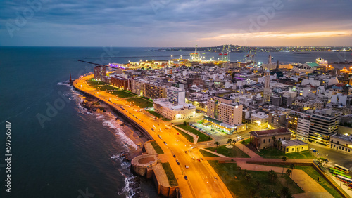 aerial above Montevideo capital city of Uruguay cityscape at night with port and modern buildings over the coastline during sunset