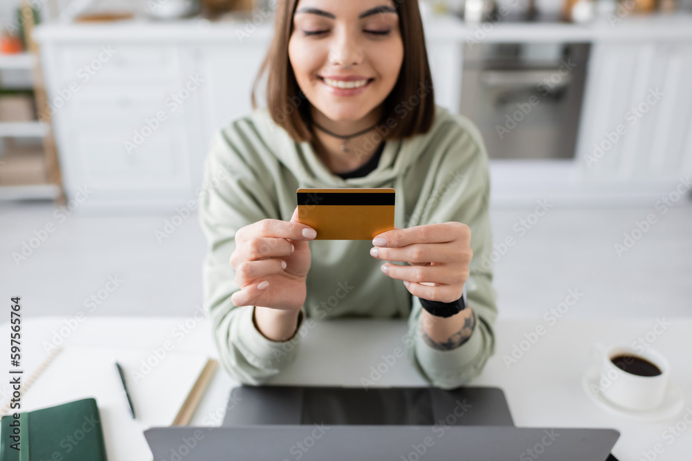 Smiling woman holding credit card near laptop and coffee on table at home. Smiling woman holding credit card near laptop and coffee on table at home.