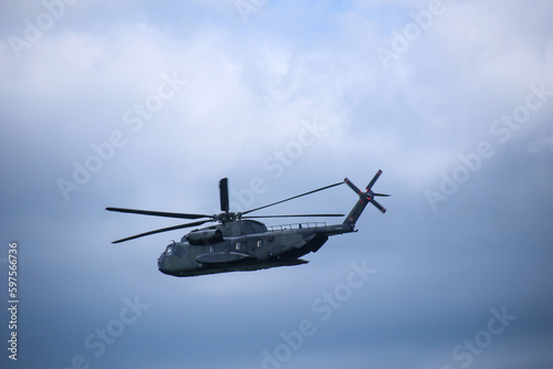 Ein militärischer Hubschrauber mit offener Heckklappe am Himmel.

