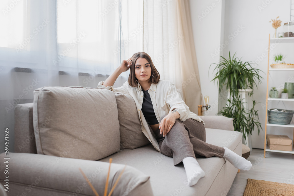 Brunette woman in casual clothes looking at camera while sitting on couch at home. Brunette woman in casual clothes looking at camera while sitting on couch at home.