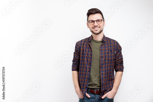Unshaved charming cheerful positive young man in glasses hold hands pockets isolated on white background