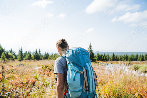 A rear view of a man with a backpack on a hike, a tourist carries a trunk with things on his back, a mountain trip, a hipster on a hike, a tuft of hair on his head.