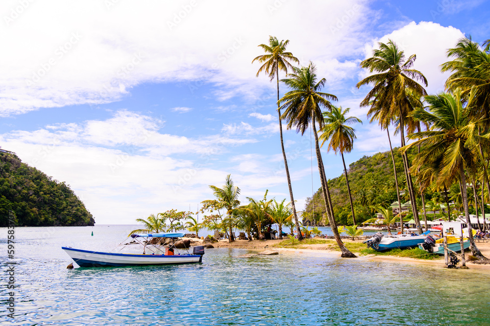 Tropical island scene at beautiful Marigot Bay in the Caribbean island of Saint Lucia, with palm trees and boats ashore on the beach.