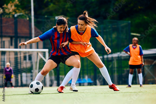 Female players tackling during soccer practice on playing field.