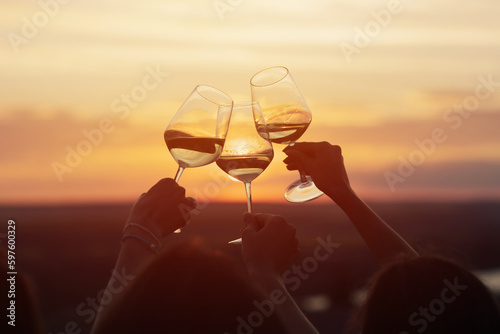 A group of girlfriends raise a toast with glasses of white wine on a sunset. Close shot.	