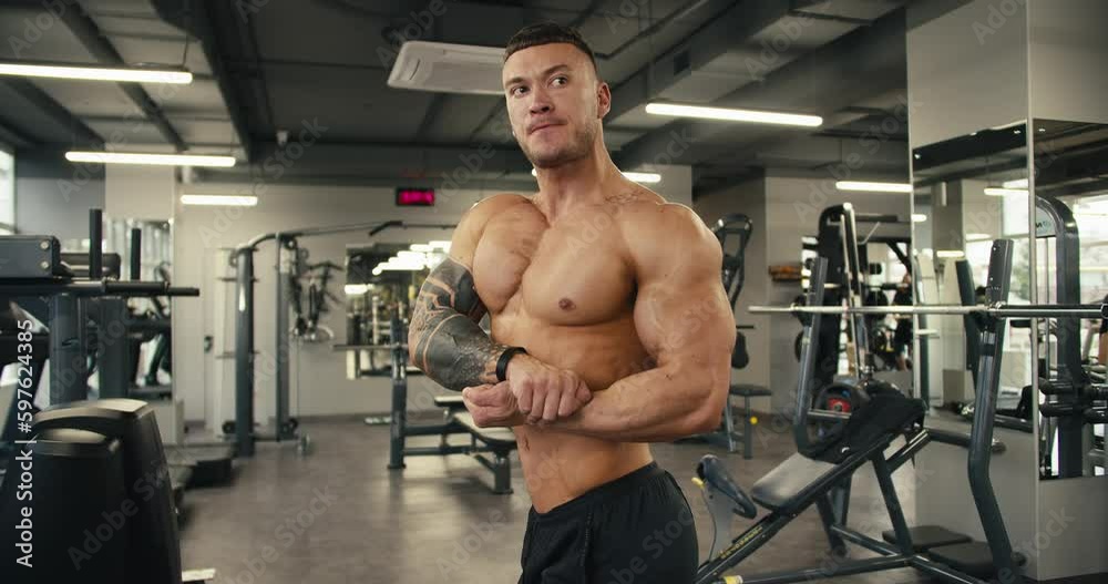 A young athlete with a naked torso poses and shows his muscles. The result of long and hard work in the fitness room A young athlete with a naked torso poses and shows his muscles. The result of long and hard work in the fitness room