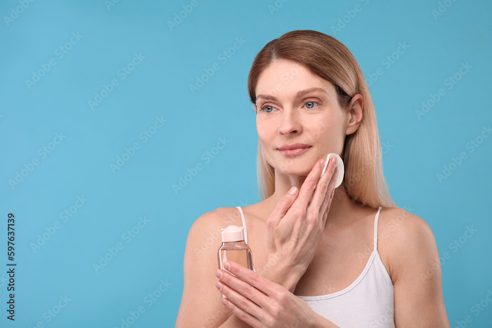 Beautiful woman removing makeup with cotton pad on light blue background, space for text Beautiful woman removing makeup with cotton pad on light blue background, space for text