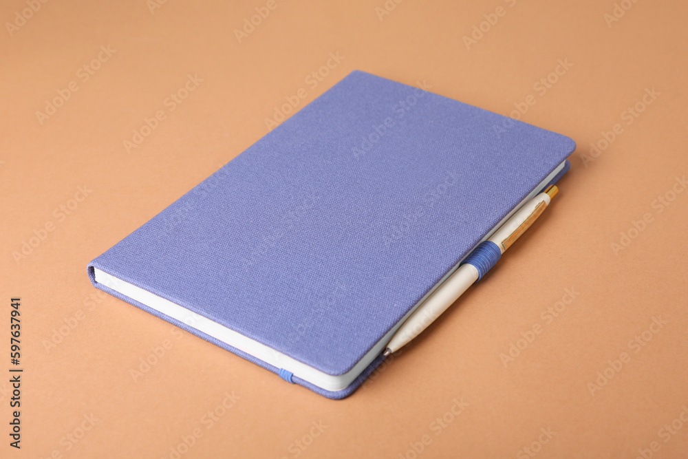 Closed blue notebook and pen on light brown background Closed blue notebook and pen on light brown background