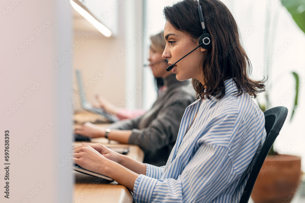 Group of female operator talking with wireless headset while searching information in laptop in the office Group of female operator talking with wireless headset while searching information in laptop in the office