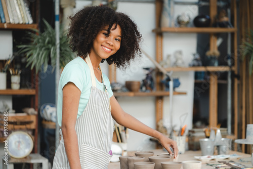 Creative afro American young woman artist molding clay form by hand finger on pottery wheel, handcraft workshop in ceramic creation studio, making a pot material in hobby and leisure with pleasure
