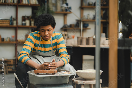 An Afro-haired potter sculpts a ceramic pot from clay on a potter's wheel. Art workshop concept, hands with clay making of a ceramic pot on the pottery wheel, hobby and leisure with pleasure concept