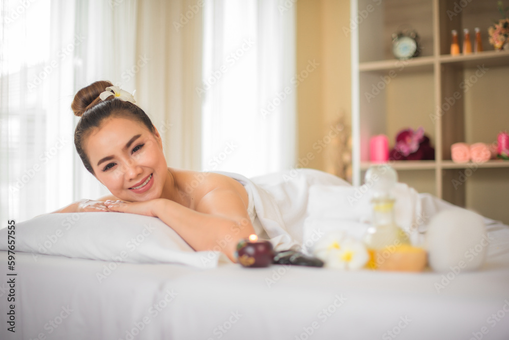 Beautiful asian woman is lying comfortably on a white bed in the spa room and there have a glass of spa oil next to her while looking to the camera in spa room. Beautiful asian woman is lying comfortably on a white bed in the spa room and there have a glass of spa oil next to her while looking to the camera in spa room.