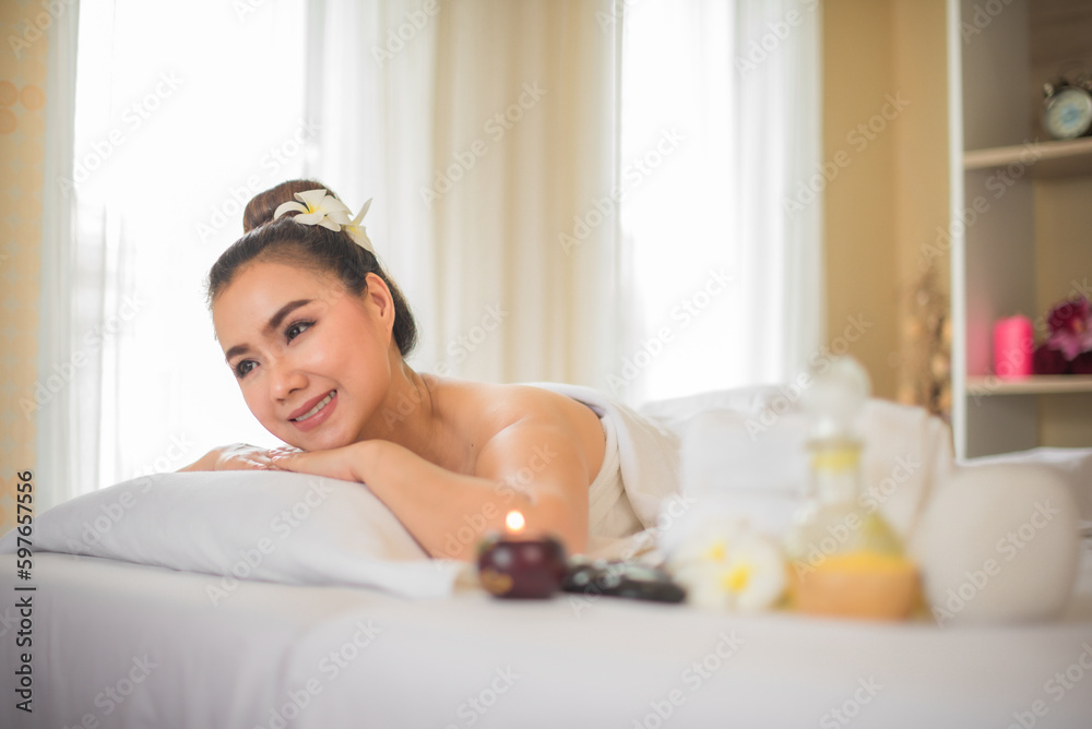 Beautiful asian woman lying on white bed while looking sideway and there have a glass of spa oil next to her in spa room. Beautiful asian woman lying on white bed while looking sideway and there have a glass of spa oil next to her in spa room.