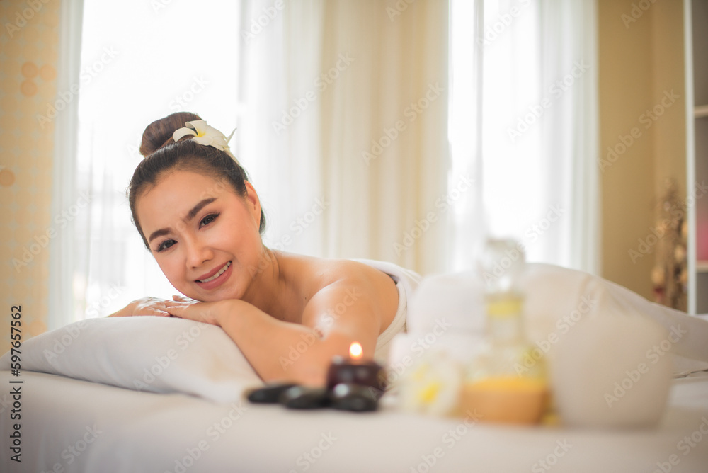 Beautiful asian woman is completely relaxed as she lying down on the comfortable bed with her hands on her chin in the spa room while looking to the camera. Beautiful asian woman is completely relaxed as she lying down on the comfortable bed with her hands on her chin in the spa room while looking to the camera.