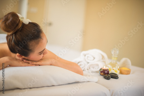 Beautiful asian woman is completely relaxed as she lying down on the comfortable bed with her hands on her chin in the spa room while looking to the spa oil.