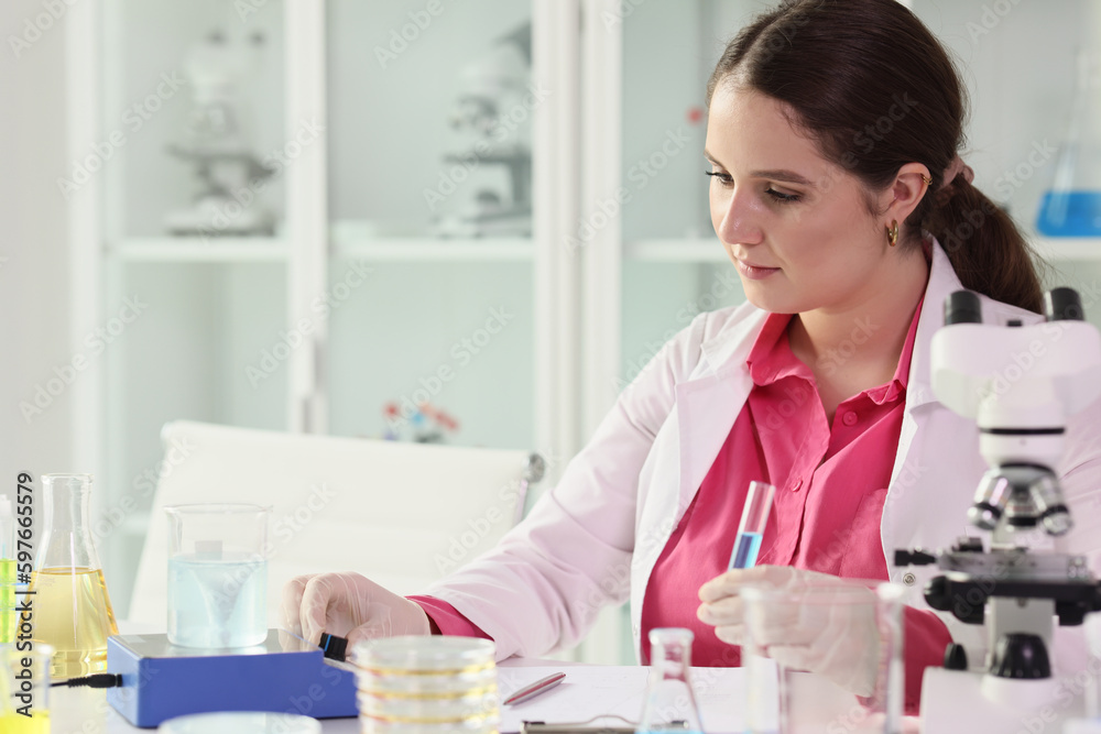 Focused brunette woman holds test tube with blue liquid Focused brunette woman holds test tube with blue liquid