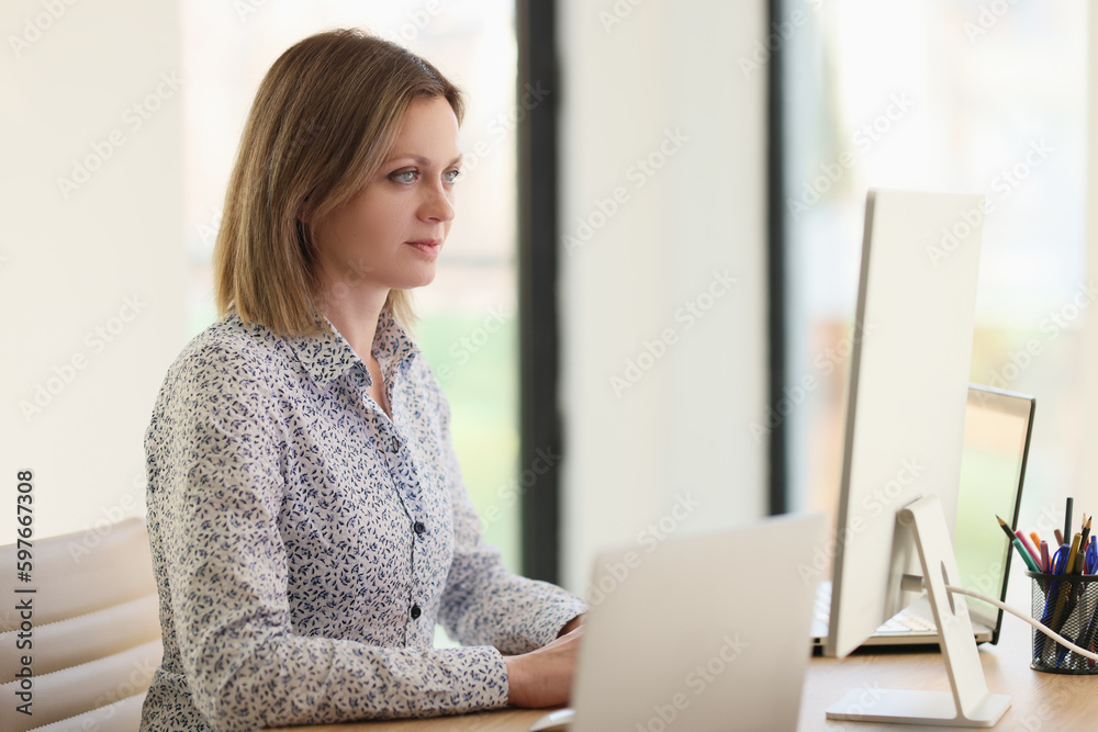 Focused woman looks at computer and laptop screens at desk Focused woman looks at computer and laptop screens at desk