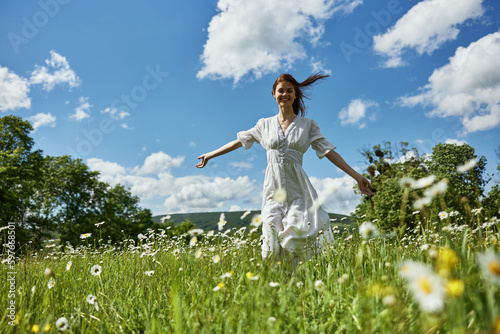 a happy woman in a light dress runs across a field of daisies towards the camera. Sunny weather, peace, happiness