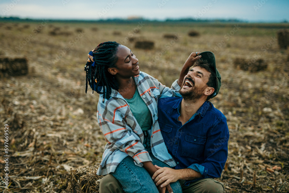 Playful multiethnic couple sitting outdoors in the countryside, a black woman sitting in a lap of a caucasian man.