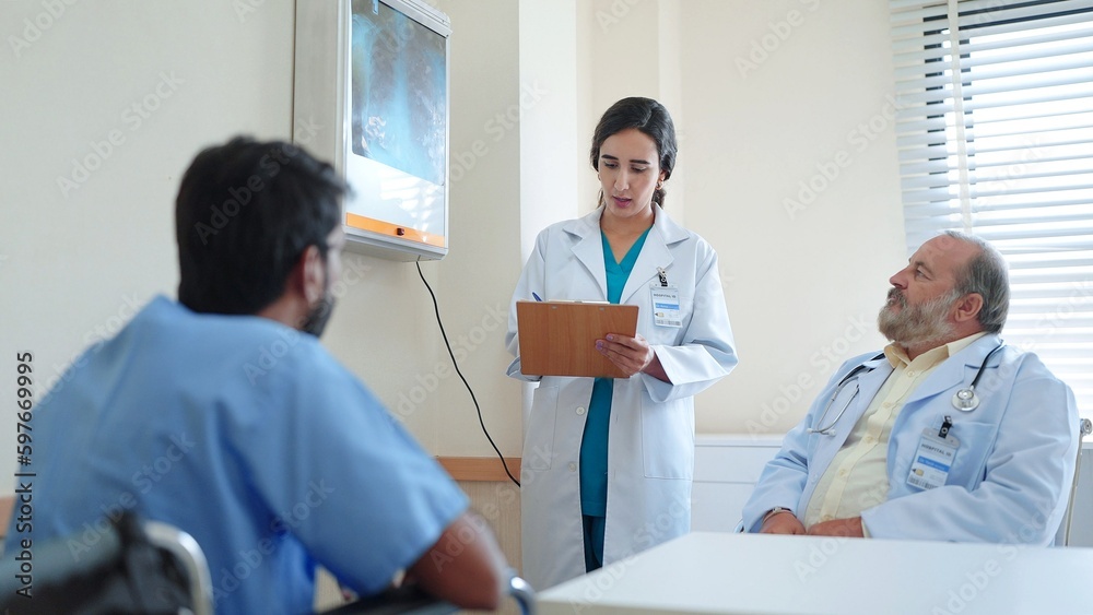 Woman medical assistant writing treatment information on clipboard senior male doctor and Indian male patient sitting there listening explaining results Woman medical assistant writing treatment information on clipboard senior male doctor and Indian male patient sitting there listening explaining results