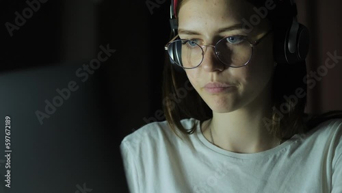 Tired teenage girl with glasses looks at the monitor, plays a game, reads, studies late at night