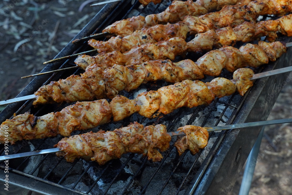 Shashlik - traditional Georgian barbecue. Closeup of raw roasted marinated meat barbecue shish kebab shashlik on steel metal skewers lying grill fire brazier with charcoal.  Making barbecue